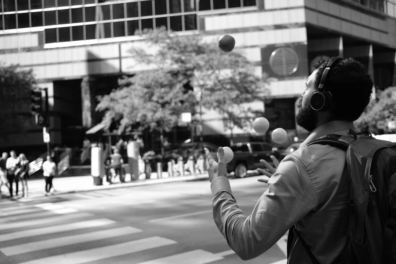 Person juggling balls, wearing headphones, backpack.